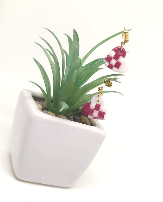 Handmade red and white Julehjerter earrings in polymer clay — with gold-plated stainless steel ball studs displayed on a plant